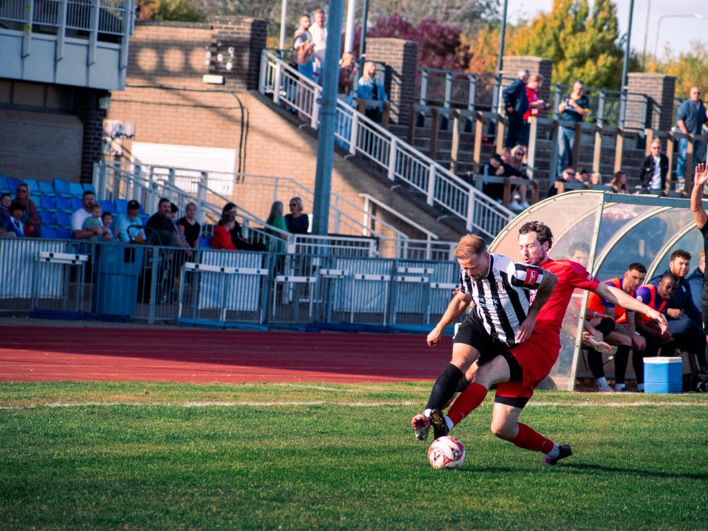 Two footballers battling for the ball on a sunlit pitch